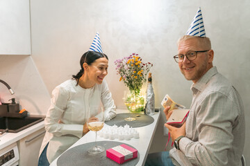 Couple Birthday Celebration Kitchen: Romantic intimate birthday celebration; happy couple in kitchen exchanging gifts; joyful moment captured.