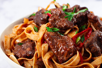 Udon noodles with Mongolian beef, green onions and vegetables, in a white plate, on a light background, homemade, no people,