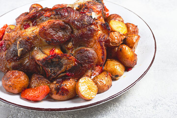 Pork knuckle baked with vegetables, new potatoes , on a white plate, homemade, no people,