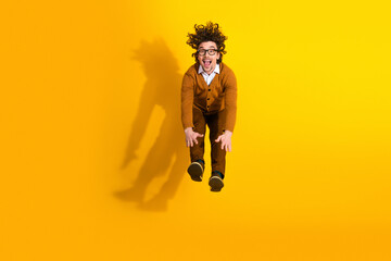 Naklejka premium Young man jumping in mid air wearing cardigan and glasses against bright yellow background smiling and having fun