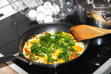 Fried eggs with tomatoes and herbs on induction stove