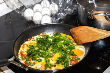 Homemade eggs with tomatoes and herbs cooking on induction stove