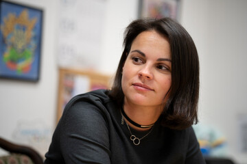 a beautiful dark-haired woman sitting at a desk in an office, looking to the side with a blurred background. Professional business scene