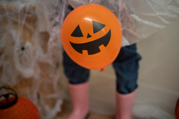 Orange balloon shaped like a pumpkin on a background with spider web and ghost legs. Funny and spooky Halloween decoration creating festive mood.