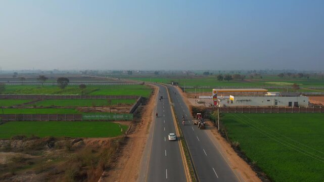 Aerial view of a road, cars, and a Shell gas station contrasting with the lush green fields, Nankana Sahib, Punjab, Pakistan.