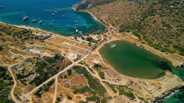 Aerial view of Knidos' ancient ruins against the turquoise sea, where boats rest in the harbor, Knidos, Mugla, Turkiye.