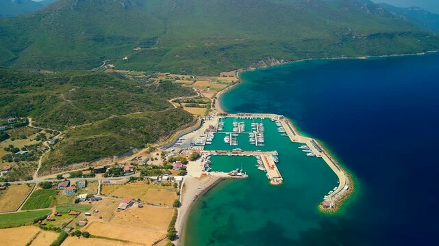 Aerial view of Kormen Marina, where turquoise waters meet the land, boats bob gently, and the green hills cascade down to the Aegean Sea, Datca, Mugla, Turkiye.
