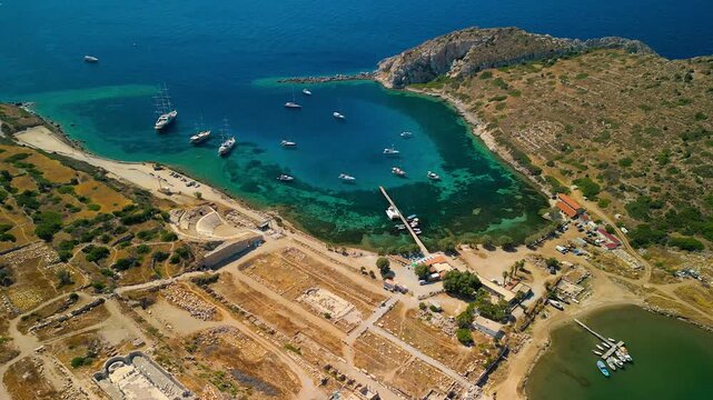 Aerial view of the ancient Knidos ruins meeting the turquoise sea, where docked boats add a touch of vibrancy, Knidos, Mugla, Turkey.