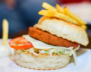 A burger with a bun, tomato, mayonise and a piece of cheese. Tomato is coming out of the burger.