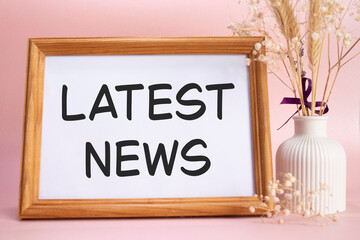 Latest News symbol. Concept words Latest News on beautiful wooden picture frame. Beautiful pink background with flower vase. Business and Latest News concept. Copy space.