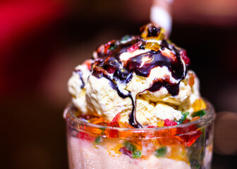 A glass of ice cream with a chocolate sauce on top. Icecream is melting on top of glass