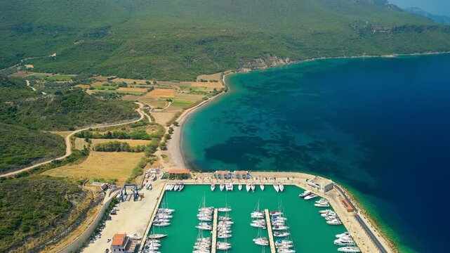 Aerial view of boats docked in Kormen Marina, where turquoise waters meet the lush green hills and sandy beach, Datca, Mugla, Turkey.