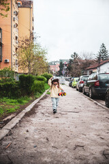 A little girl in a yellow raincoat is walking confidently alone on the sidewalk