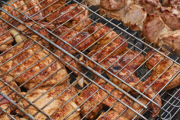 Juicy pieces of chicken are grilled in a metal grill over hot coals. The ruddy crust and smoky aroma emphasize the atmosphere of a picnic and a summer vacation in nature.