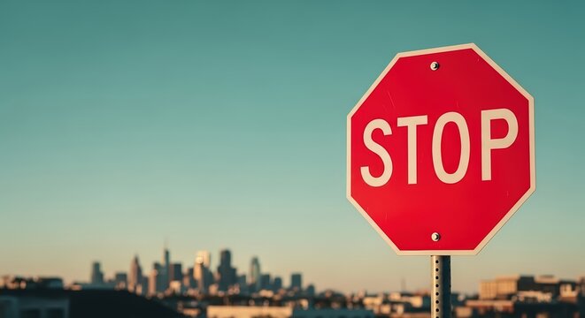 Red octagonal stop sign stands prominently against a clear blue sky, with a blurred city skyline in the background, emphasizing traffic regulations and safety awareness