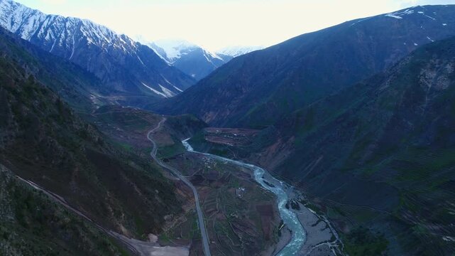 Aerial view of a winding river carving through a valley with mountains reaching towards the sky, creating a symphony of greens and blues, Naran, Khyber Pakhtunkhwa, Pakistan.