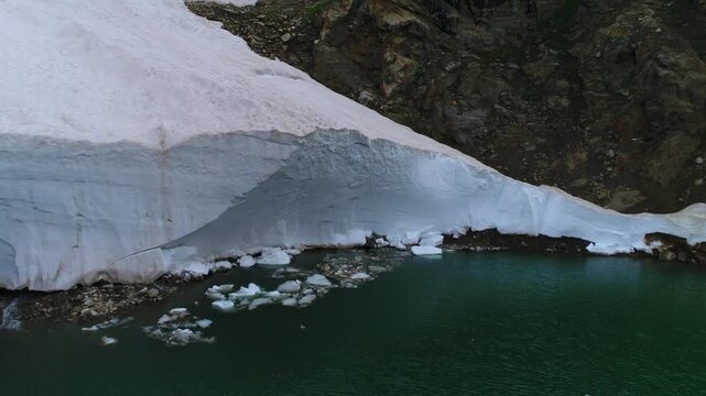 Aerial view of the contrast between the stark white snow against the dark, rugged mountain and the emerald lake, Naran, Khyber Pakhtunkhwa, Pakistan.