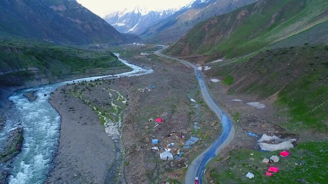 Aerial view of the river snaking through rocky terrain, flowing alongside a winding road dotted with tents, Naran, Khyber Pakhtunkhwa, Pakistan.