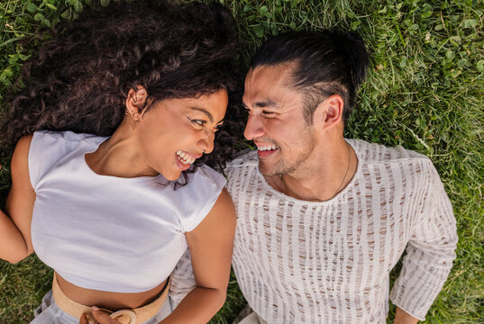 Smiling diverse couple lying on grass enjoying connection