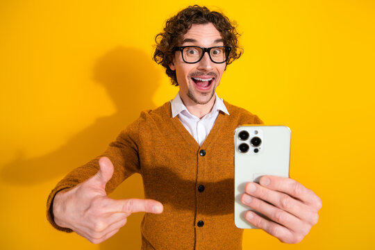 Selfie cheerful man with glasses in orange cardigan takes a lighthearted video call against yellow background