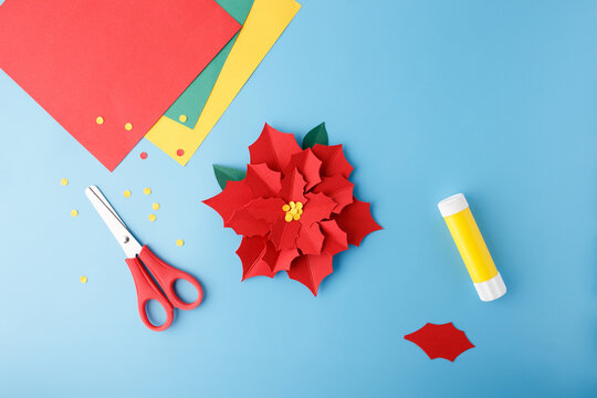 Flat lay of handmade paper poinsettia flower and supplies for DIY crafts. Ideal for educational publishers, preschool content creators, kids toy packaging, hobby courses promotion,