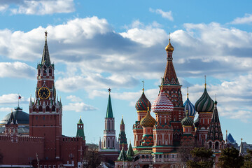 A landscape with a cathedral with colorful onion domes and the Kremlin tower against a bright cloudy sky. A classic view of Russian architecture
