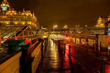 Footpath and road entrance leading underground to Waverley Railway station on a wet night, Edinburgh. The Balmoral hotel is in the background