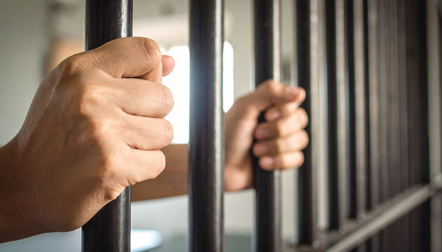 close up de las manos de un reo o condenado en prision agarrado a los barrotes de una carcel, concepto de violacion de la ley y condena por delitos