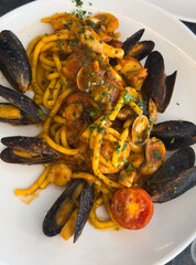 A round plate of Italian seafood pasta garnished with half a tomato on a trattoria table in Italy