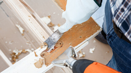 Carpenter using heat gun and wood scraper removes paint from old wooden window. Construction industry, carpentry. Restoration. 