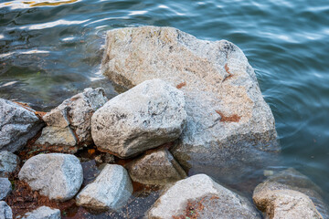 Granite rocks on the shore of Štrbské Pleso mountain lake in the High Tatras, with clear water washing around the stones.