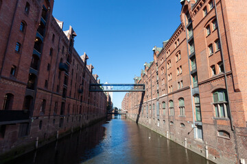 Classic view of the historic Speicherstadt warehouse district in Hamburg, featuring red brick facades reflected in the waters of the canal under a clear blue sky