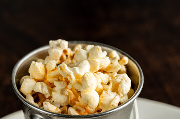 A close-up, high-angle shot of fluffy, seasoned popcorn served in a small, rustic metal cup against a dark background, perfect for a movie snack or appetizer.