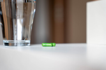 Green Herbal Capsules with Water on White Surface