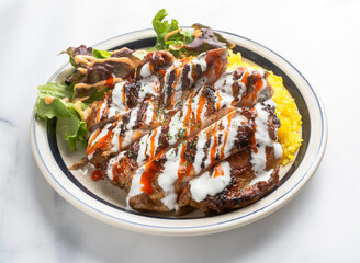 Grilled chicken and rice drizzled with creamy white and hot sauce, paired with fresh greens. Perfect for healthy eating and dining.