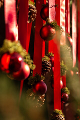 A festive Christmas decoration with red ribbons, pinecones, and shiny ornaments, warmly lit by sunlight to create a natural and cozy holiday atmosphere.