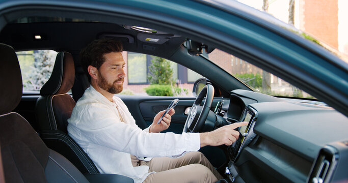 Modern man setting up navigation and music on phone inside stylish vehicle. Concept of technology, travel, connection, and modern lifestyle - Powered by Adobe