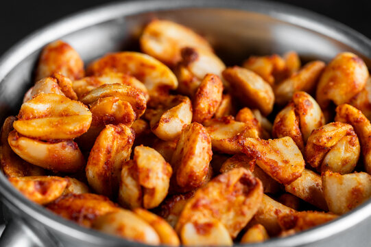 Close-up of vibrant, spicy chili-seasoned roasted peanuts in a metal bowl, captured with shallow depth of field for a delicious, crunchy snack visual.