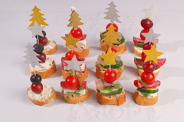 An assortment of various Canapes with tomatoes, pate, mozzarella cheese, salami, herring, olives, and grapes on a marble table. Christmas and New Year's dishes, a set of appetizers for festive table