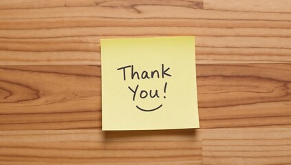 A simple yellow sticky note with 'Thank You!' handwritten in black ink, placed on a wooden surface, celebrating Thank You Note Day.