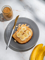 Peanut butter toast and banana on a dark plate on a marble background with fruits