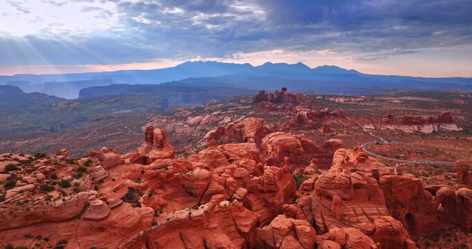 Beautiful red rocks with rounded tops in the dry desert. Sunbeams go through the cloudscape covering the sky. Aerial view. Arches National Park, Utah, USA.