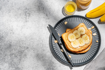 Peanut butter toast and banana on a black plate on a gray background with nuts