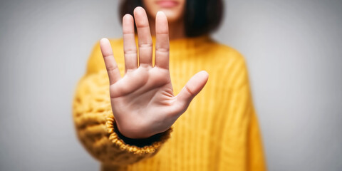Obraz premium Woman extends hand in stop gesture, signaling refusal, restriction, and personal boundaries. Cropped close up, neutral background