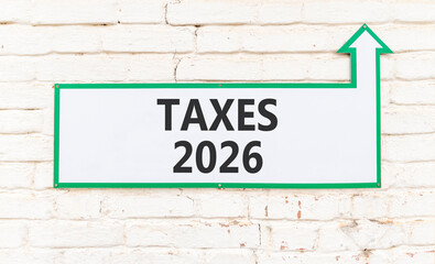 Fototapeta premium Taxes 2026 new year symbol. Concept words Taxes 2026 on beautiful white sign with arrow. Beautiful old white brick wall background. Business and taxes 2026 new year concept. Copy space.
