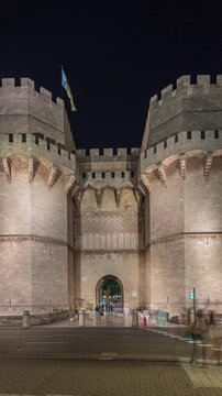 Panorama showing Serrans Towers (Torres de Serranos) night timelapse in Valencia, Spain. A grand medieval gate from the city's ancient walls. Traffic on the street with crossing near historic landmark