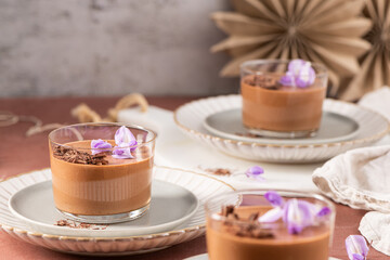 Multiple glasses of creamy chocolate mousse, garnished with delicate purple flowers and chocolate shavings, artfully arranged for a sweet moment.