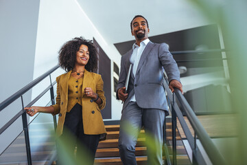 Obraz premium Happy Professionals Descend Modern Office Stairway in Stylish Business Attire, Conveys Confidence and Teamwork