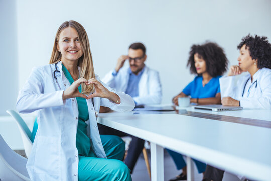 Friendly Doctor Forms Heart Gesture During Health Team Meeting in Modern Conference Room - Powered by Adobe