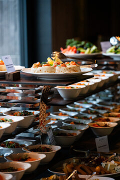 A variety of fresh dishes displayed on a buffet table at a catered event, featuring salads, appetizers, and hot meals arranged in a professional food service setup